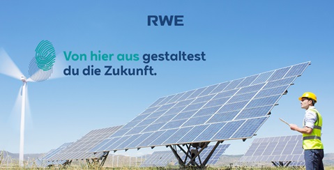 Ein Mann steht neben Solarpanelen auf einem Feld, während ein Windrad im Hintergrund sichtbar ist.