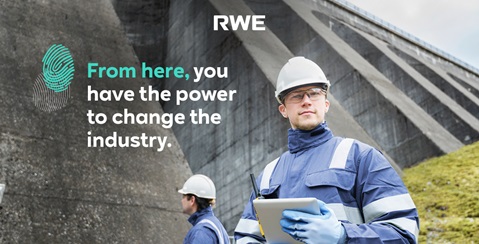 Ein Arbeiter in blauer Arbeitskleidung und Helm hält ein Tablet vor einem Staudamm. Die Umgebung ist grün und industriell.