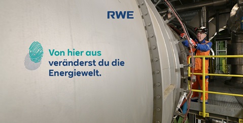 Ein Techniker in orangefarbener Schutzkleidung arbeitet an einer grossen Maschine in einem Energieanlagenbetrieb.