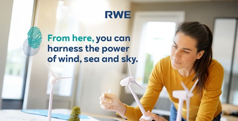 A woman in a yellow sweater works on a table with small wind turbine models and a plant.