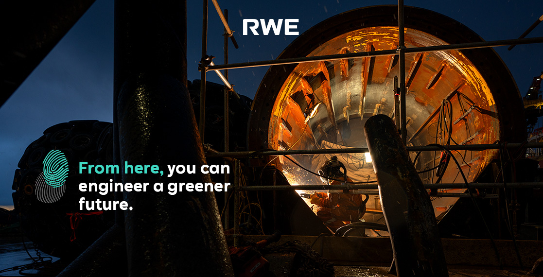A worker in an orange suit operates inside a large, cylindrical machine, with soft lighting illuminating the dark surroundings.