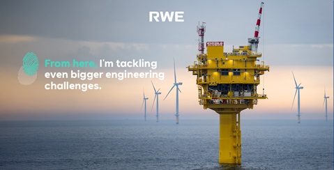 A yellow offshore platform stands in the sea, with wind turbines visible in the background.
