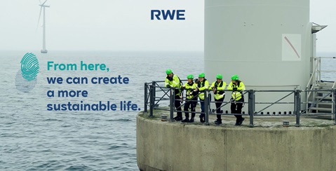 A team of workers in bright yellow safety jackets stands on a platform beside a wind turbine over the water.