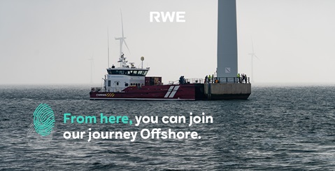 A red vessel is docked at a quay. In the background, wind turbines are visible in the mist. People are working at the quay.
