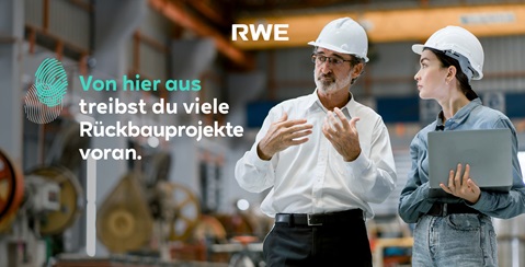 A man and a woman are engaged in a conversation in an industrial setting. Both are wearing safety helmets and discussing deconstruction projects.