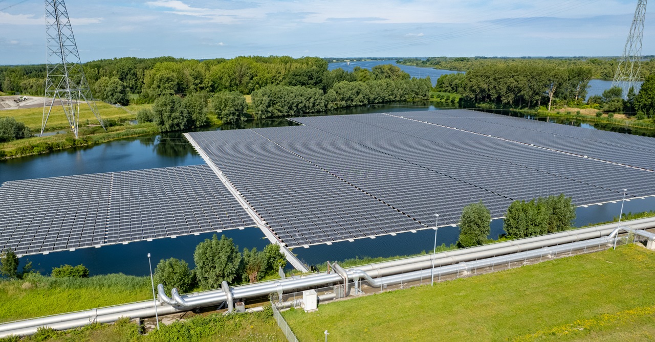 A large solar panel array floats on water, surrounded by green trees and a power line in the distance.