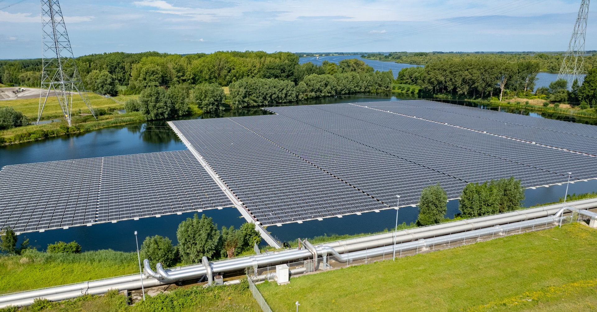 Eine große Solaranlage schwimmt auf Wasser, umgeben von grünen Bäumen und einer Hochspannungsleitung in der Ferne.