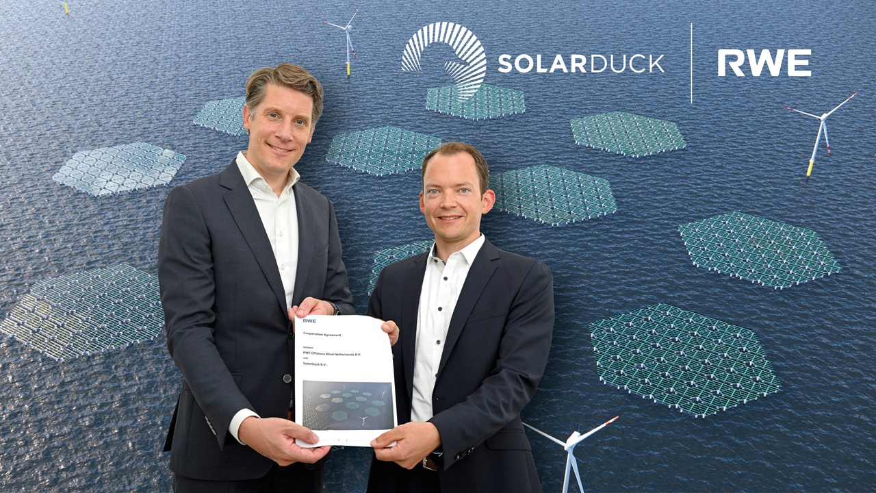 Two professionals holding a cooperation agreement with solar panels and wind turbines in the background.