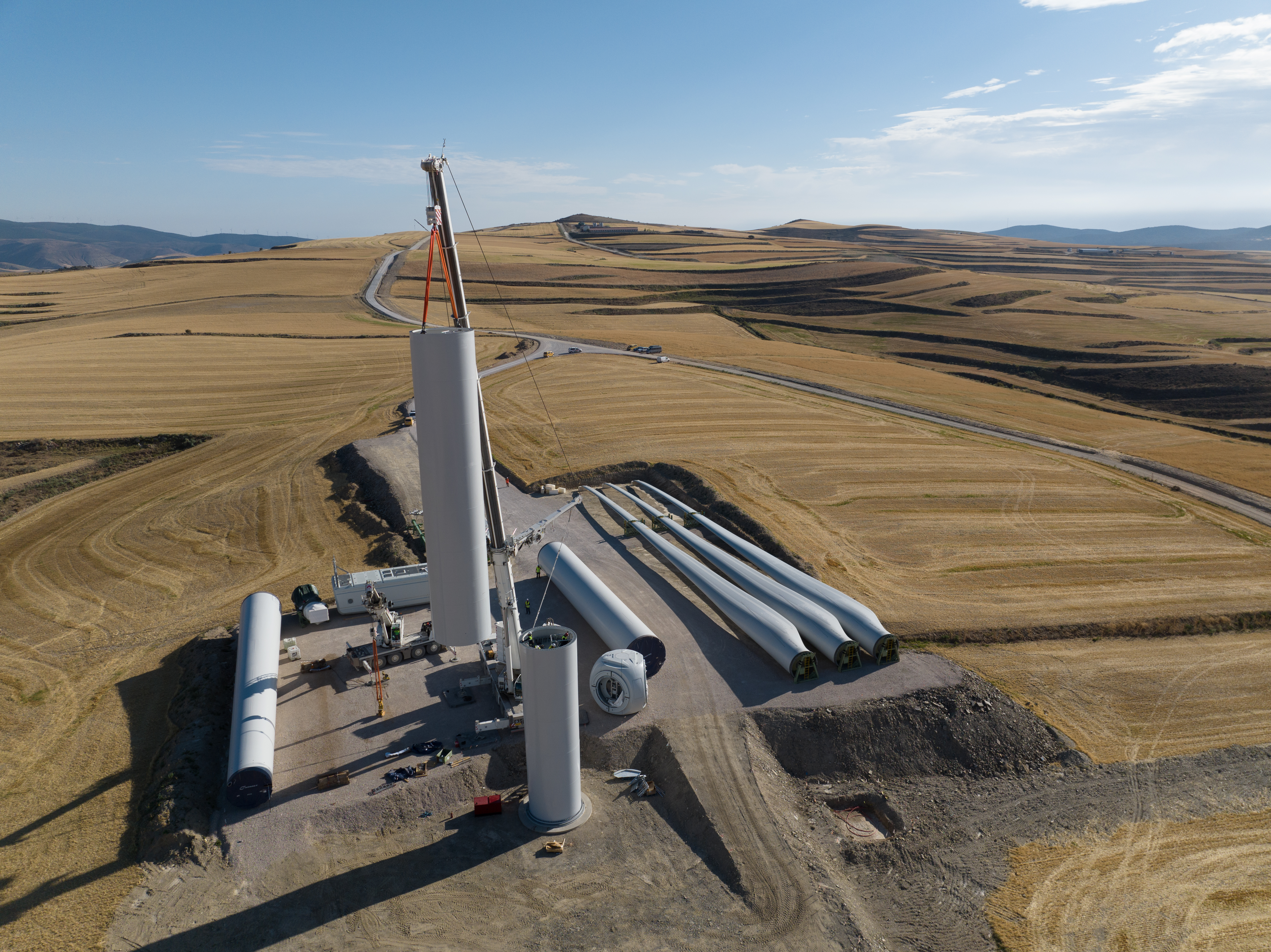An aerial view of a wind turbine under construction, with large blades and other equipment on a rural landscape.