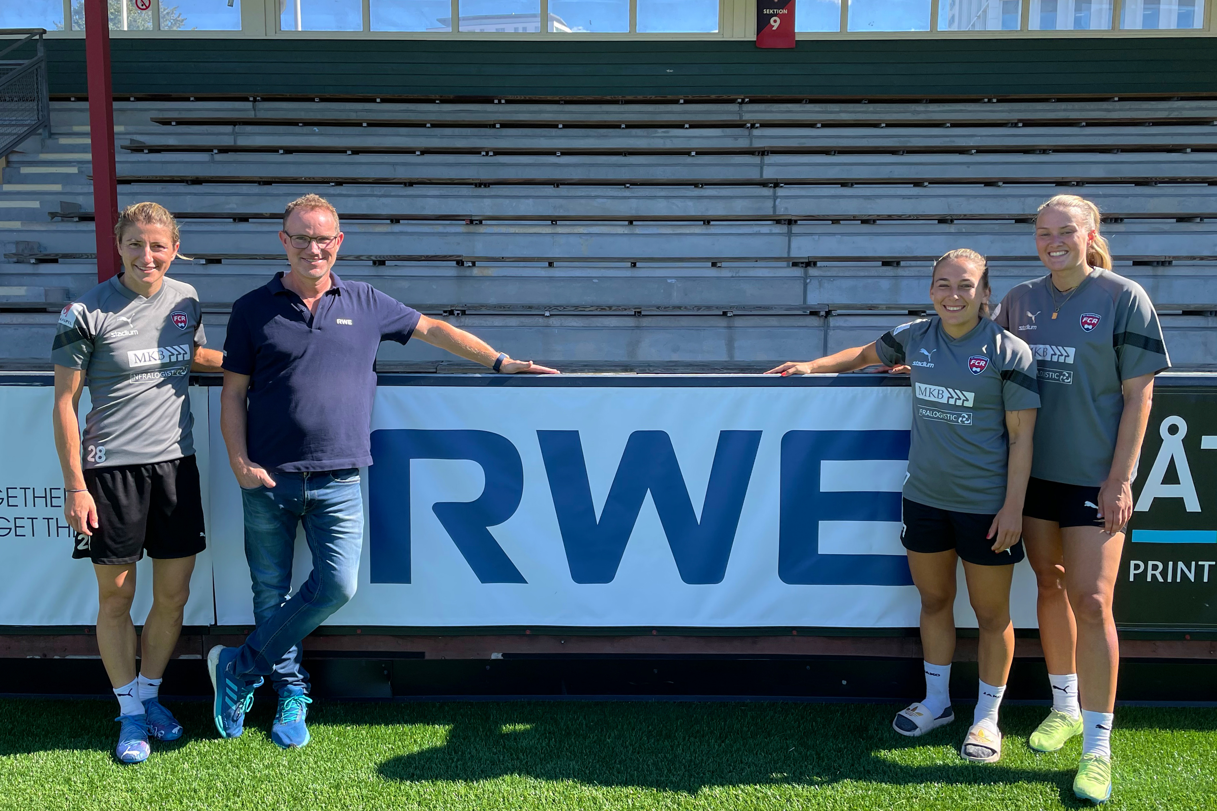 A group photo featuring athletes in sports kits, posing beside a large RWE banner in a stadium setting.
