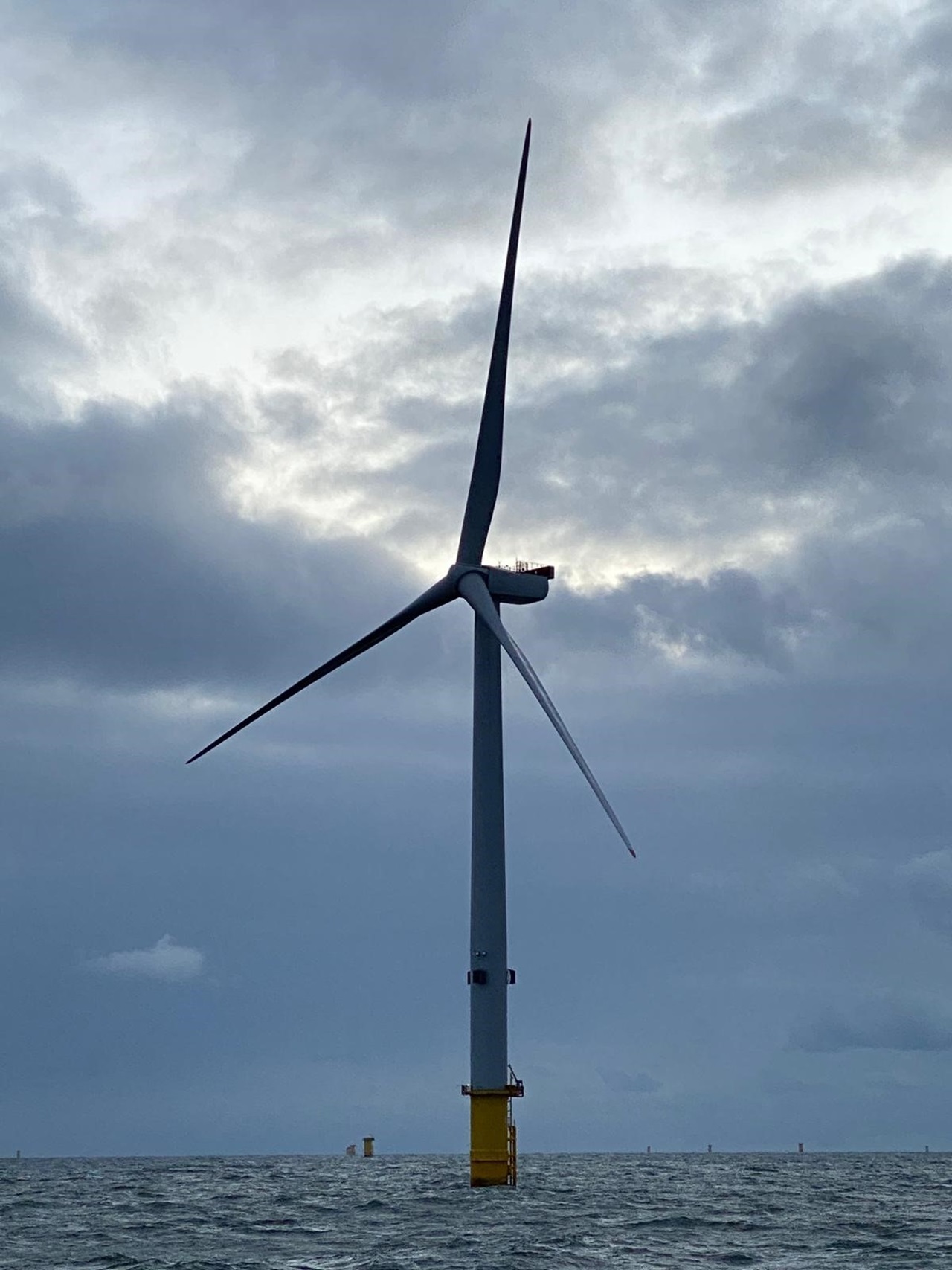 A tall wind turbine stands in the sea under a cloudy sky, showcasing renewable energy technology.