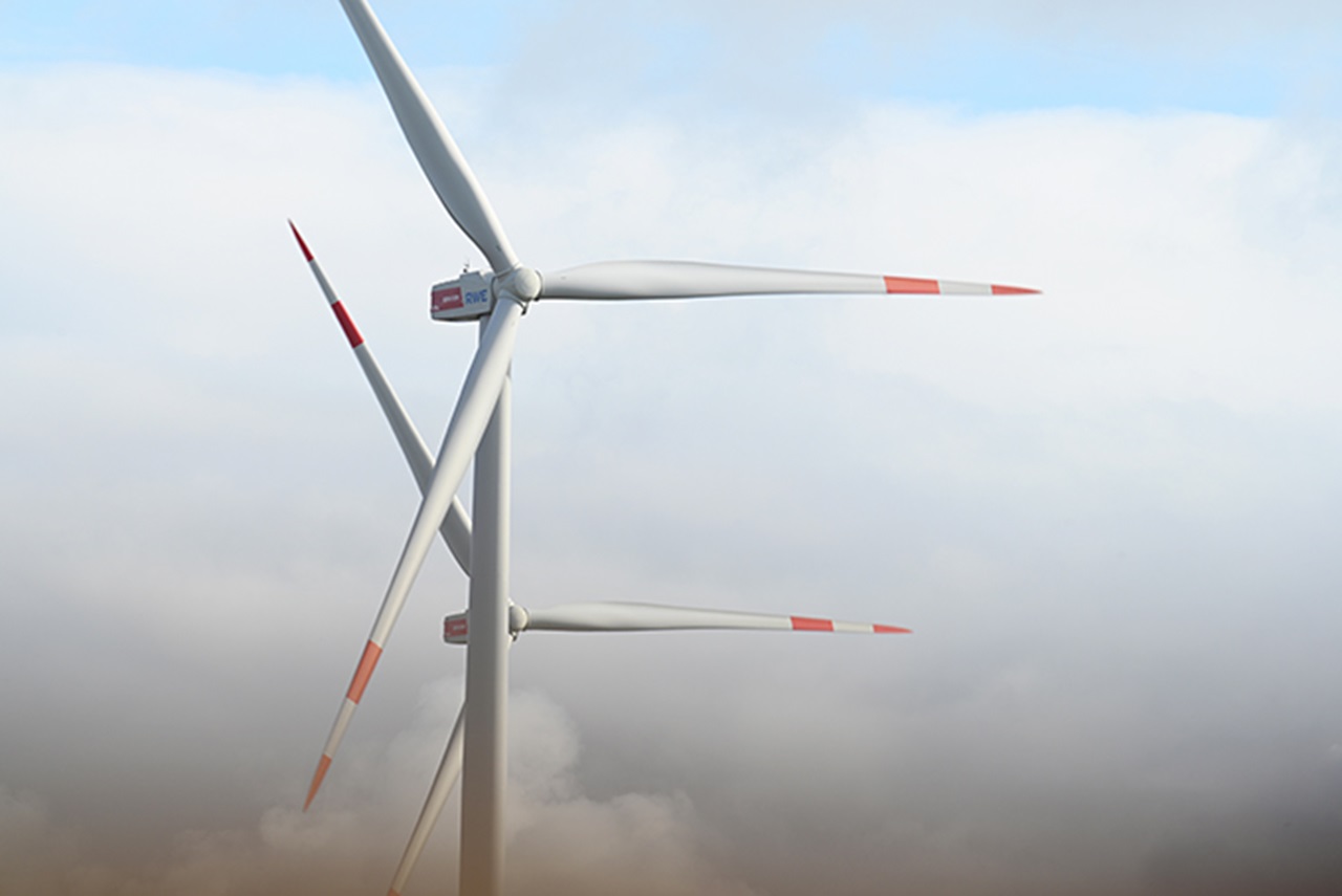 Drei Windkraftanlagen mit rot-weißen Markierungen, teilweise von Wolken verdeckt, vor einem klaren blauen Himmel.