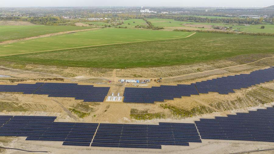 Aerial view of a large solar farm with numerous solar panels on a grassy landscape.