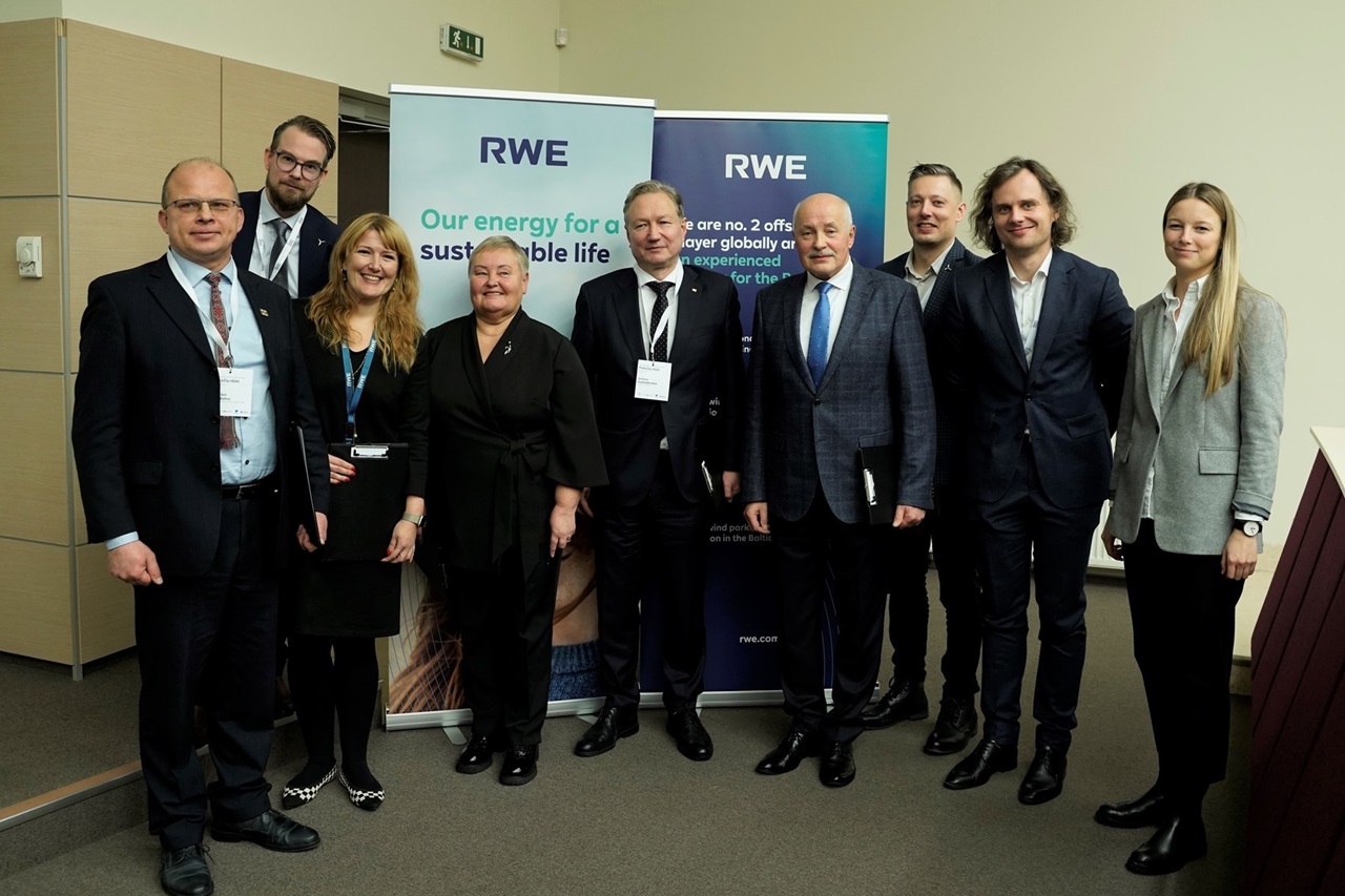 A group of professionals posing for a photo at an event, with RWE banners in the background promoting sustainable energy.