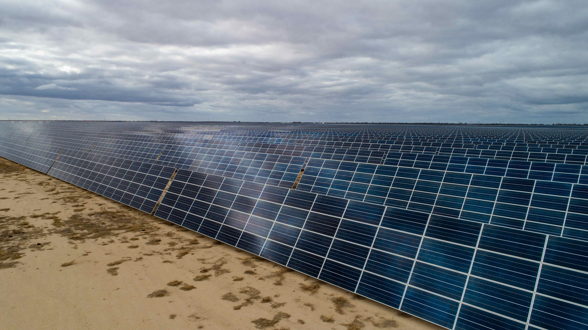 Eine riesige Solarfarm mit Reihen von Solarpanelen vor einem bewölkten Himmel, auf sandigem Boden.