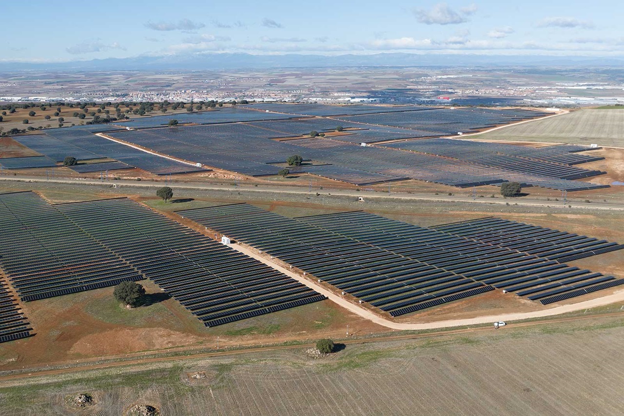 Luftaufnahme einer großen Solaranlage mit zahlreichen Solarzellen, die in Reihen über eine grüne Landschaft angeordnet sind.