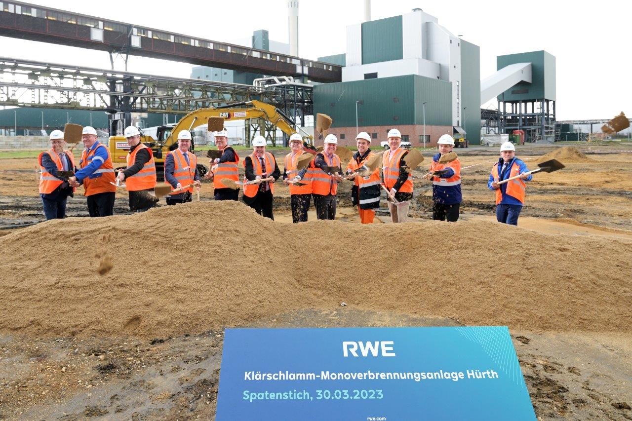 Eine Gruppe von Personen in Sicherheitswesten nimmt an einer Grundsteinlegung auf einer Baustelle teil.