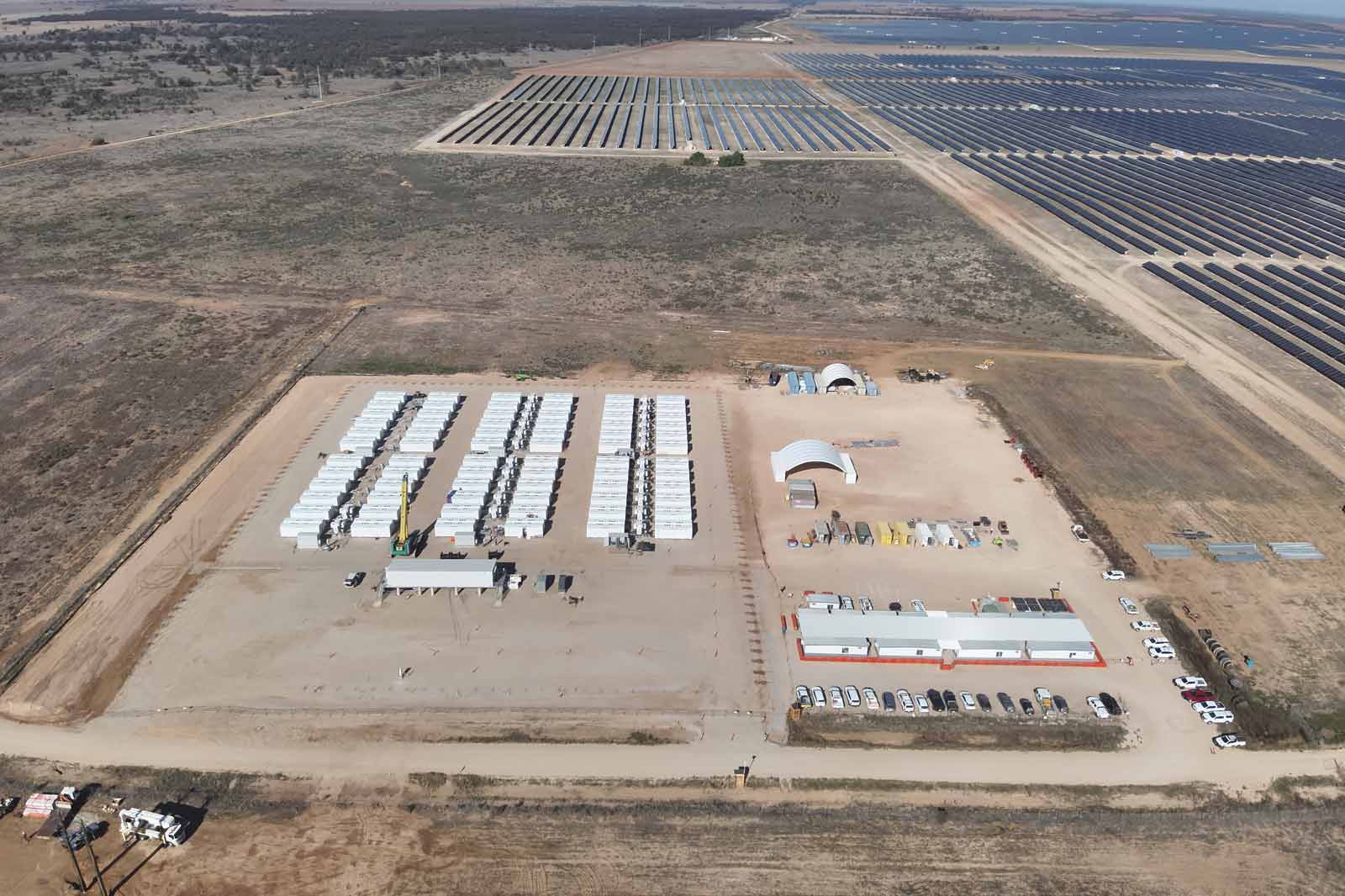 Aerial view of a solar farm featuring numerous solar panels and storage containers in a vast, open landscape.