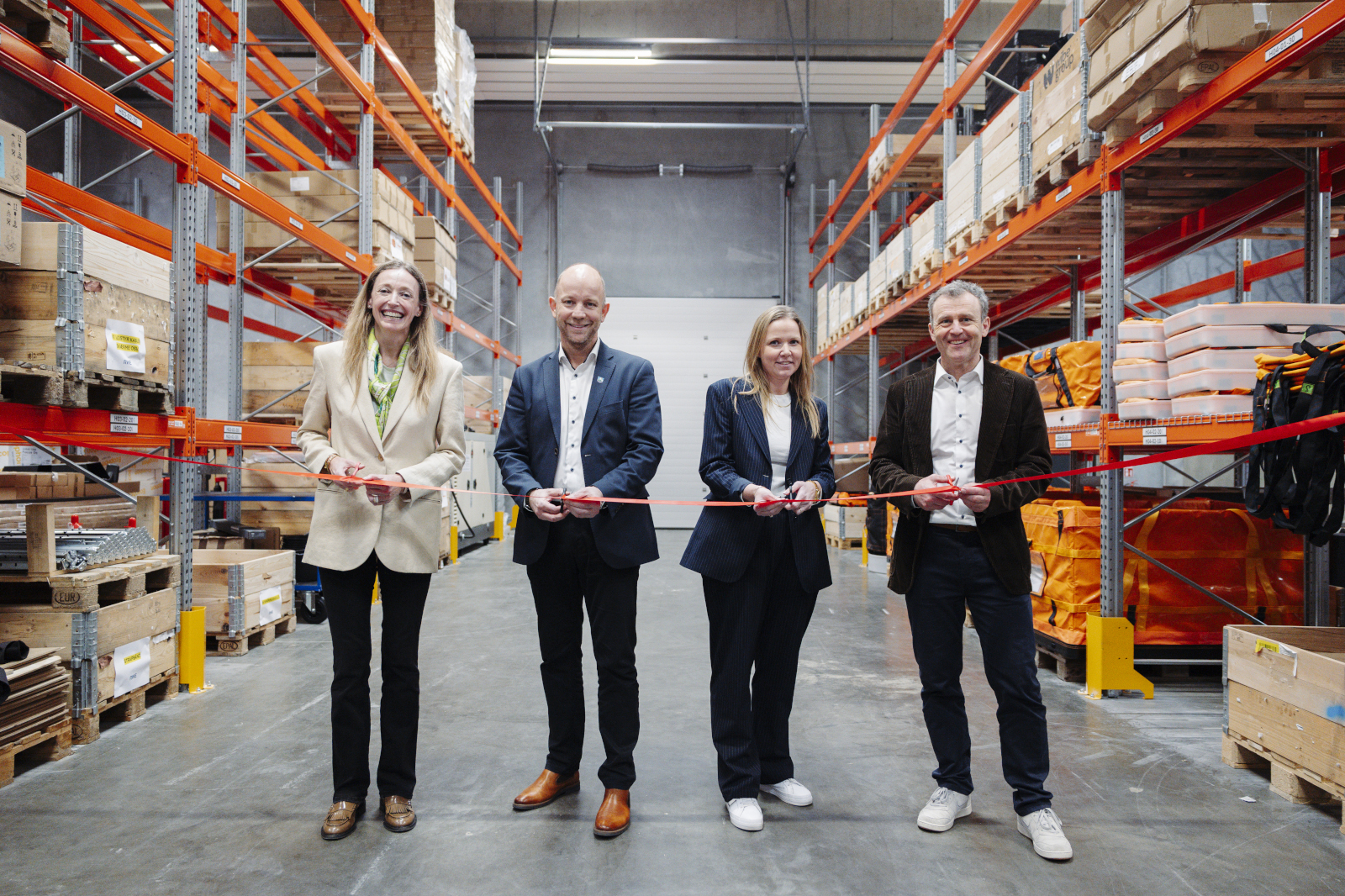 Four people stand in a warehouse cutting a red ribbon, symbolising an official opening event.