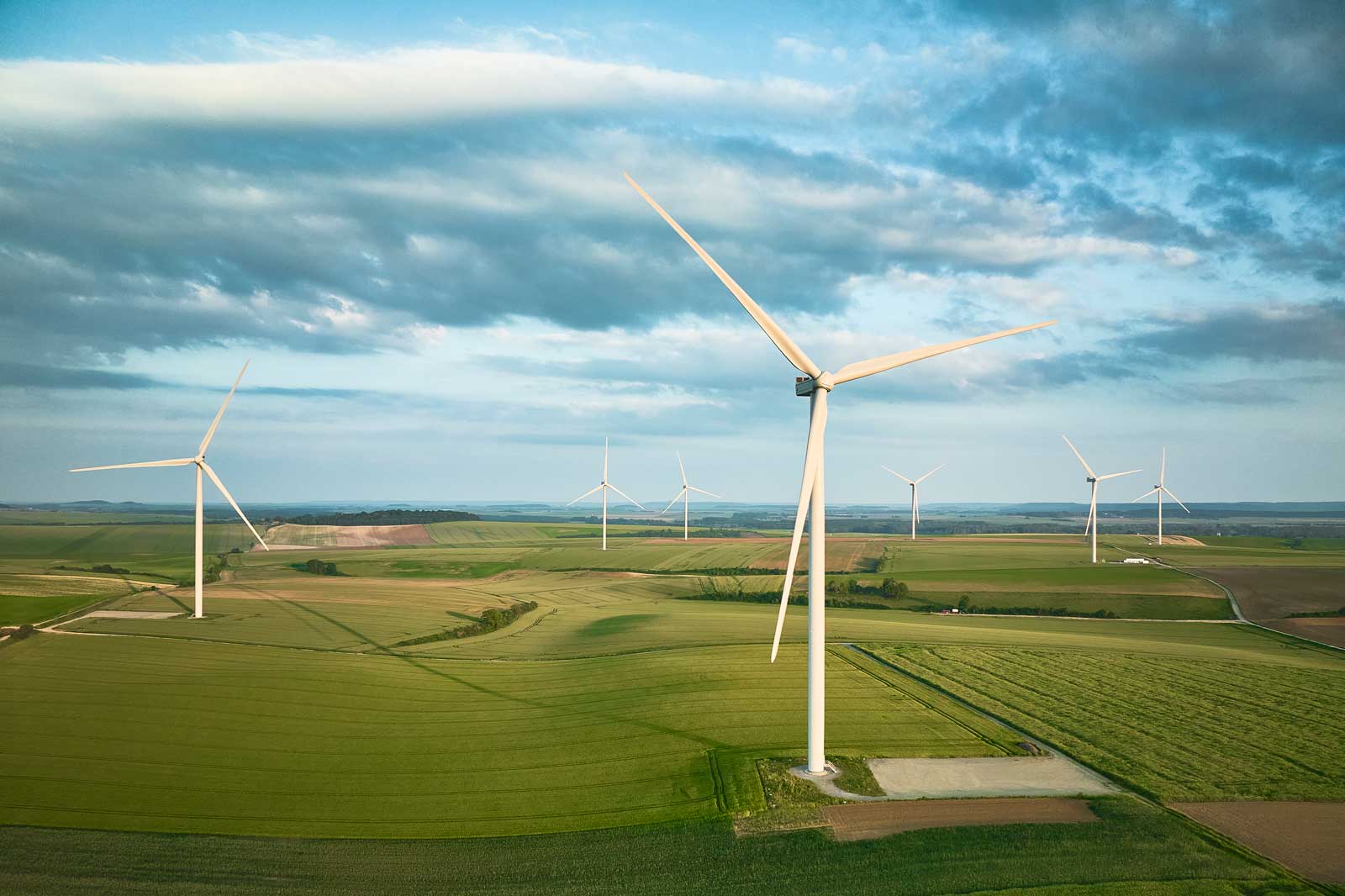 Aerial view of several white wind turbines on green fields under a cloudy sky, highlighting renewable energy sources.