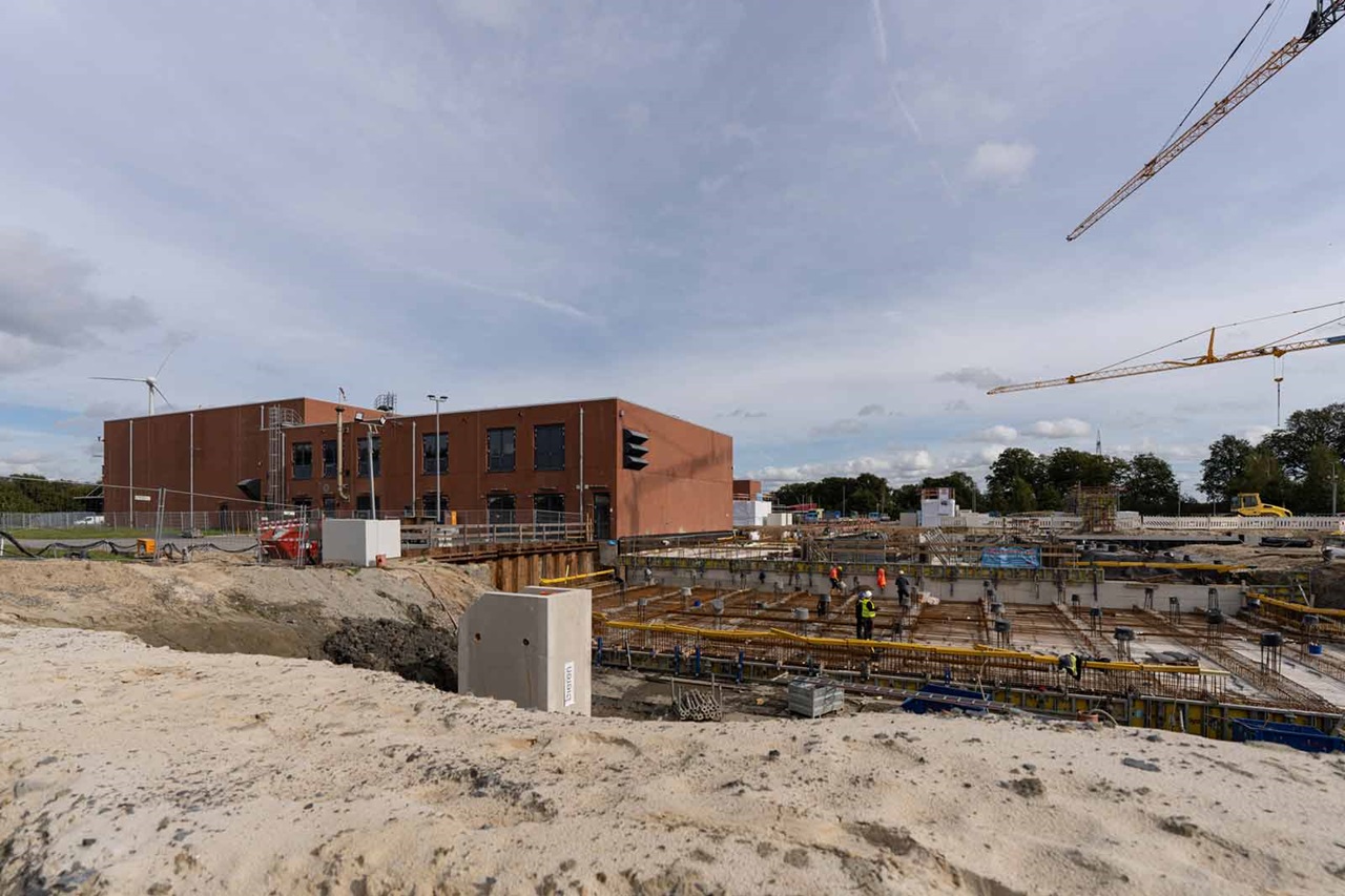 Eine Baustelle mit einem großen Gebäude im Hintergrund und Bauarbeitern, die an den Fundamenten arbeiten.