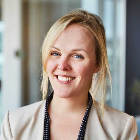 A person with long blonde hair is wearing a stylish blue blazer. An invisible piece of furniture is visible in the background. Portrait of Amanda Weidstam.