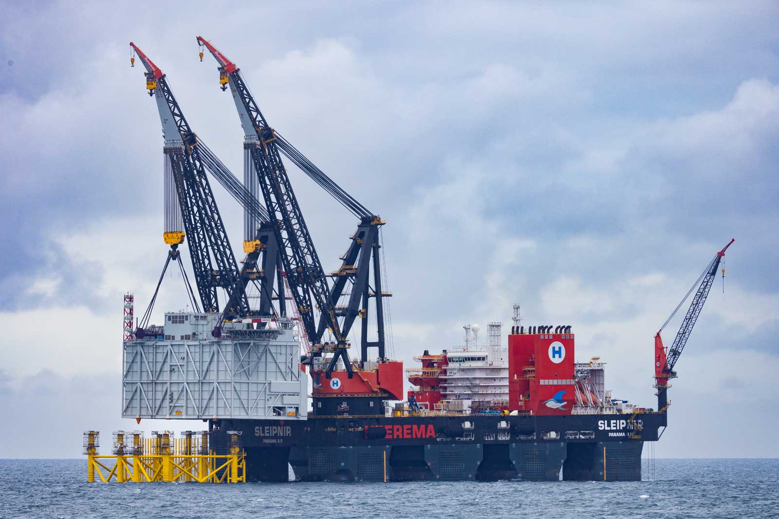 A floating crane vessel lifts a large structure module in the sea under a cloudy sky.