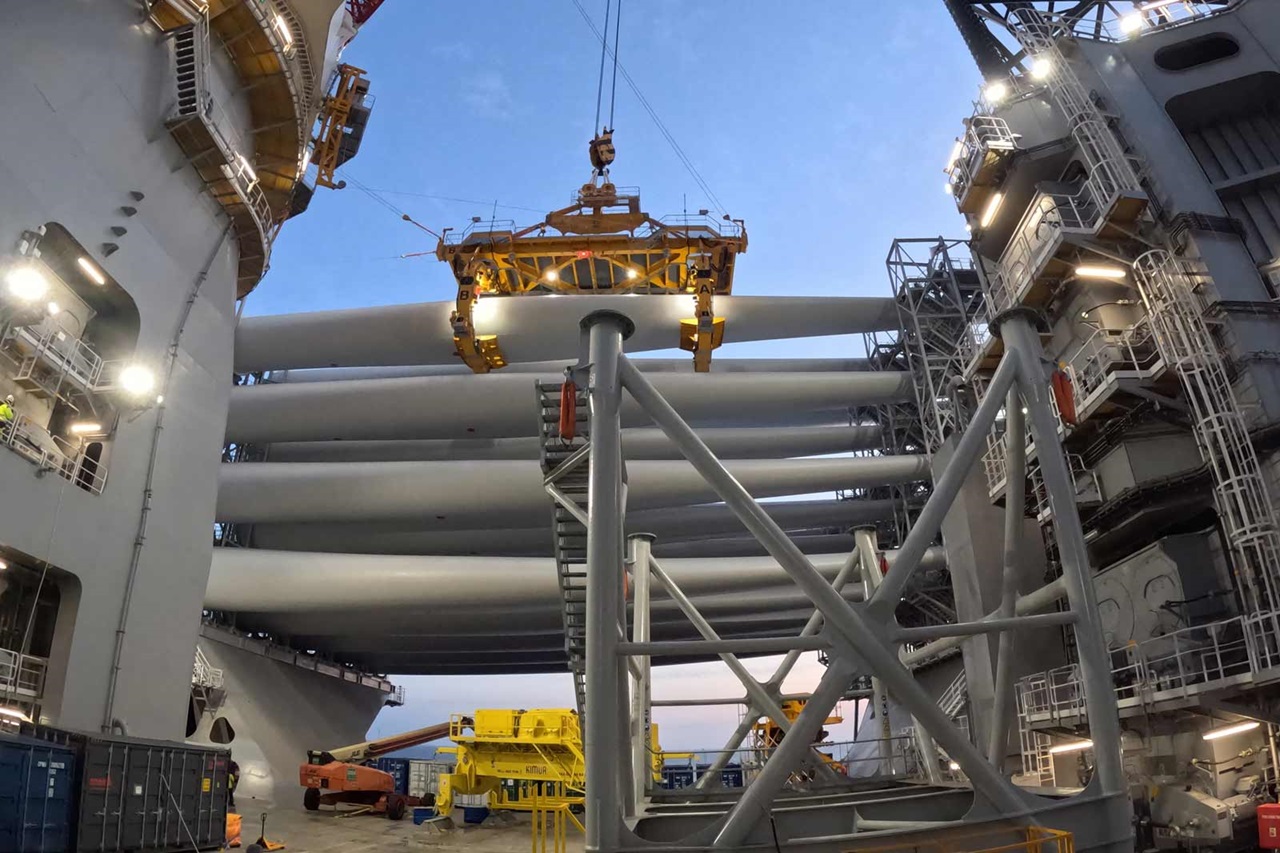 Ein Kran hebt große Rohre auf einer Offshore-Plattform an, umgeben von verschiedenen Maschinen und Beleuchtung.