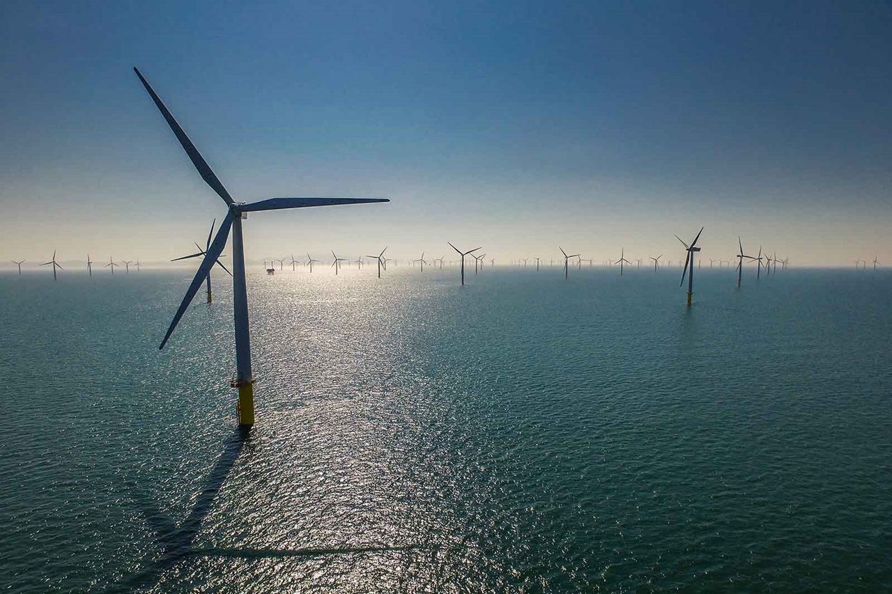 A vast offshore wind farm with numerous wind turbines on the water, reflecting sunlight under a clear blue sky.