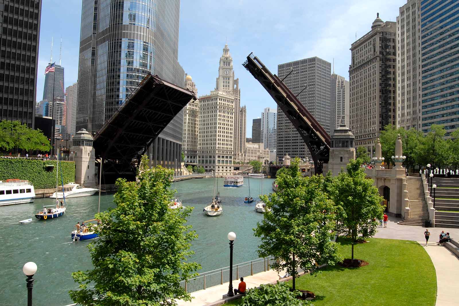 A Chicago river scene featuring a raised bridge, boats on the water, and tall buildings lining the banks.