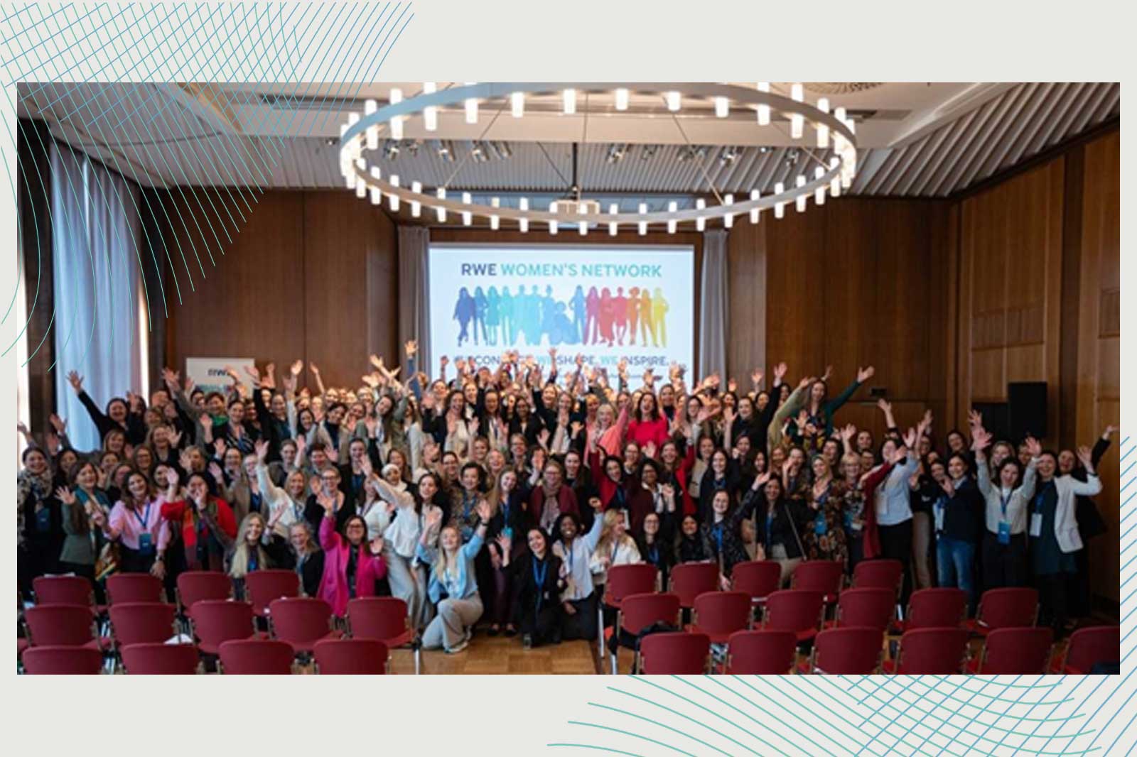A large group of people are raising their hands in a room with a banner of the RWE Women's Network in the background.