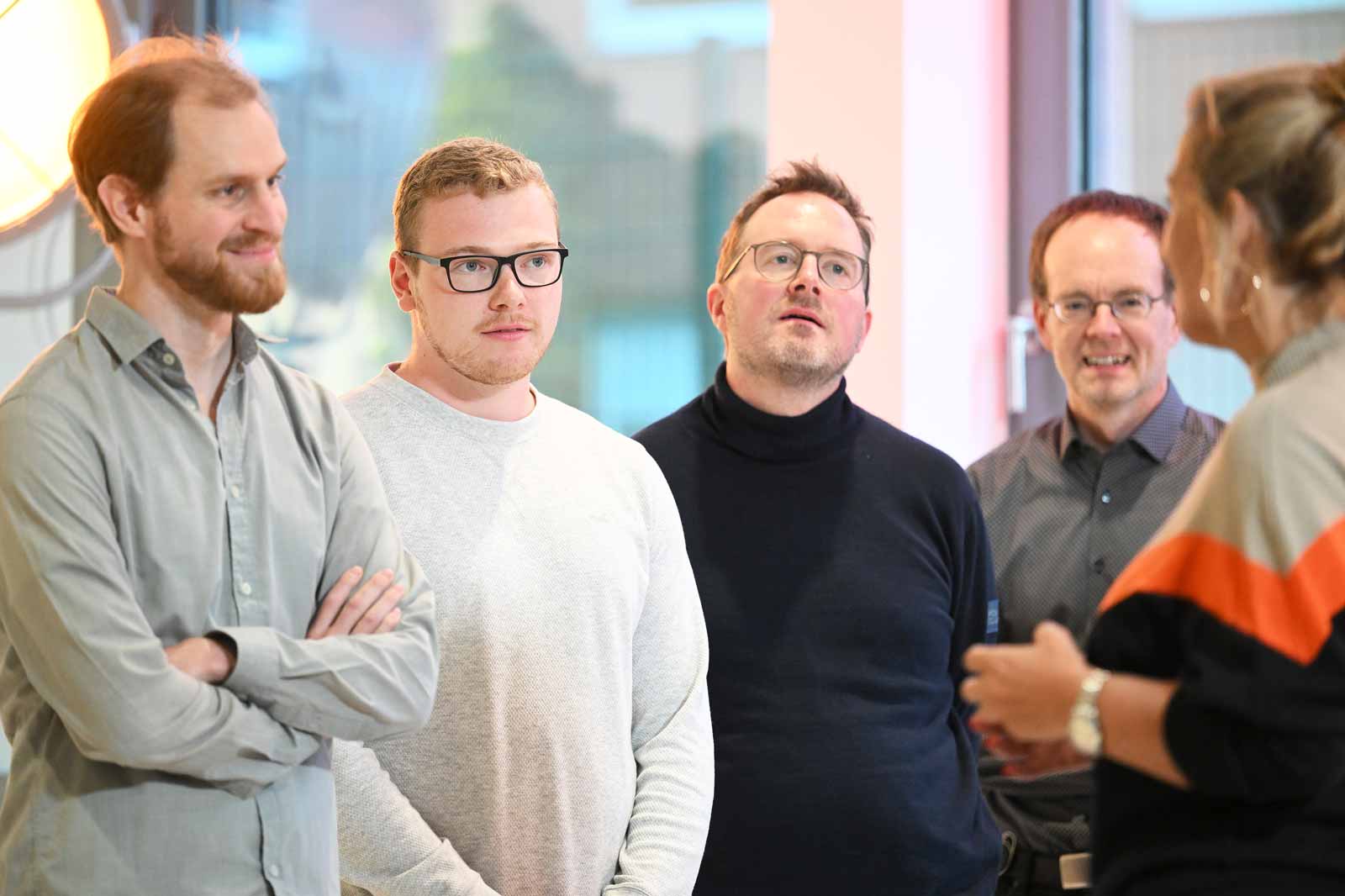 A group of men and a woman standing in a modern space, surrounded by soft light.