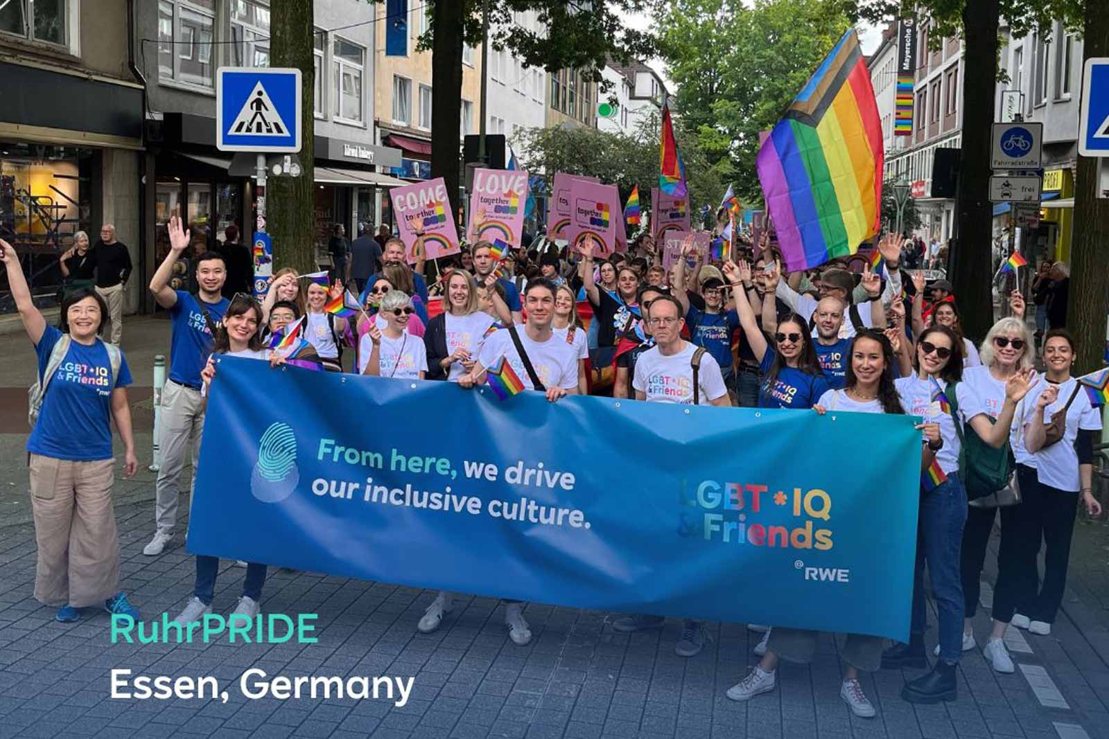 Eine Gruppe von Menschen mit Regenbogenflaggen feiert bei der RuhrPride in Essen, Deutschland, während sie ein Banner halten.
