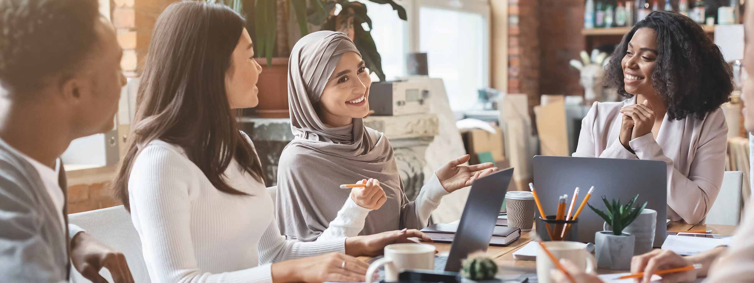 Eine Gruppe von Personen in einem modernen Büro diskutiert am Tisch über einen Laptop und Notizen.