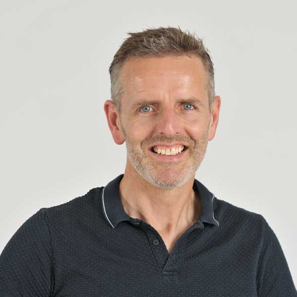 A person wearing a dark polo shirt with a collar, standing against a plain background. Portrait of Maurice Paulussen.