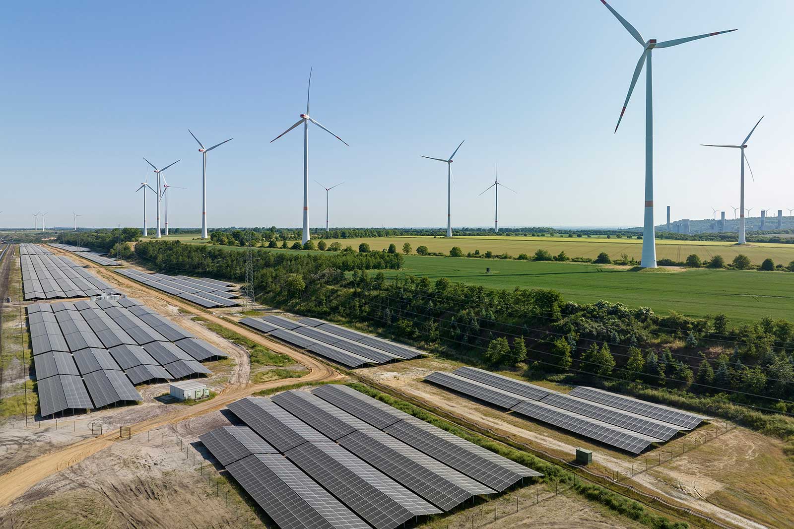 A landscape featuring solar panels in the foreground and wind turbines in the background under a clear sky.