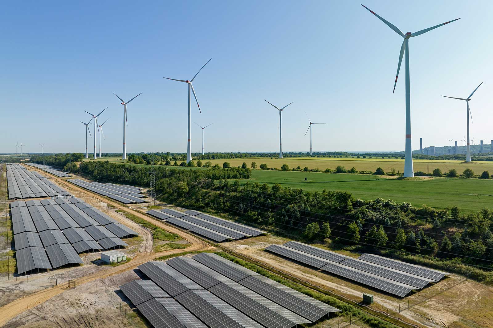 Eine Ansicht von Windkraftanlagen und Solarpanelen in einer ländlichen Umgebung an einem klaren Tag.