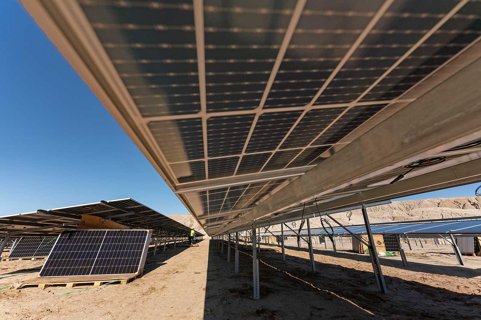 Eine Reihe von Solarpanelen, die in einem sonnigen Gebiet aufgestellt sind, mit einem klaren blauen Himmel im Hintergrund.