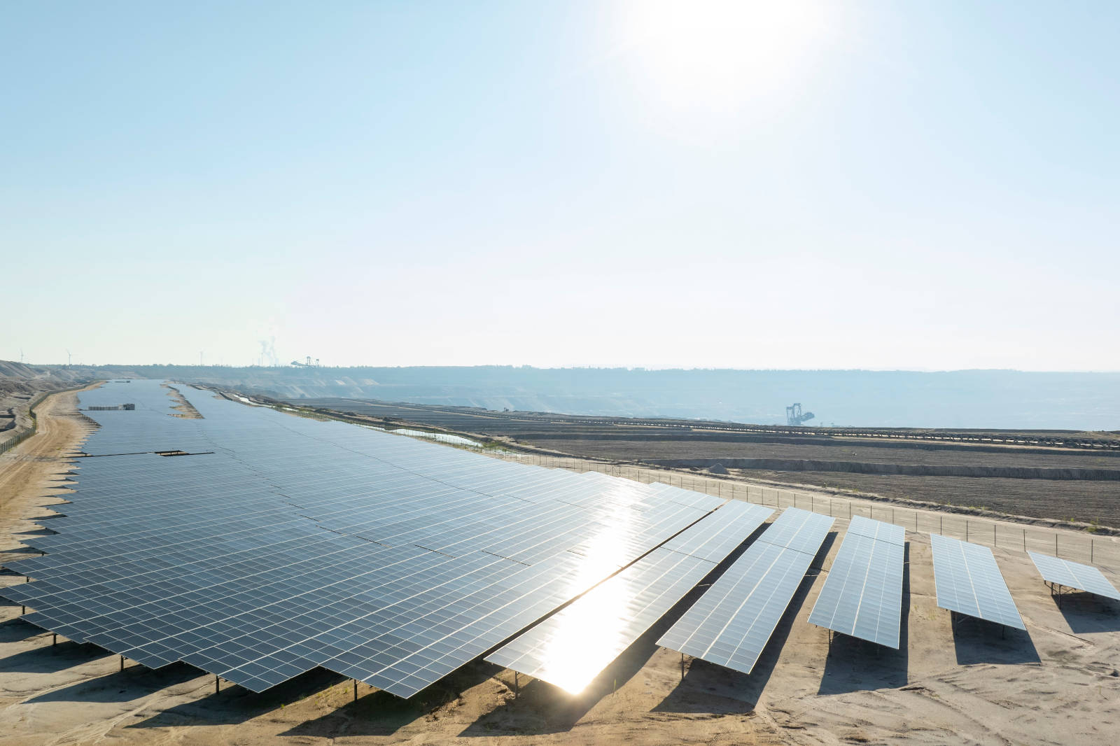 Ein weites Solarpanelfeld unter einem klaren blauen Himmel, das Sonnenlicht reflektiert, mit entfernten Hügeln im Hintergrund.