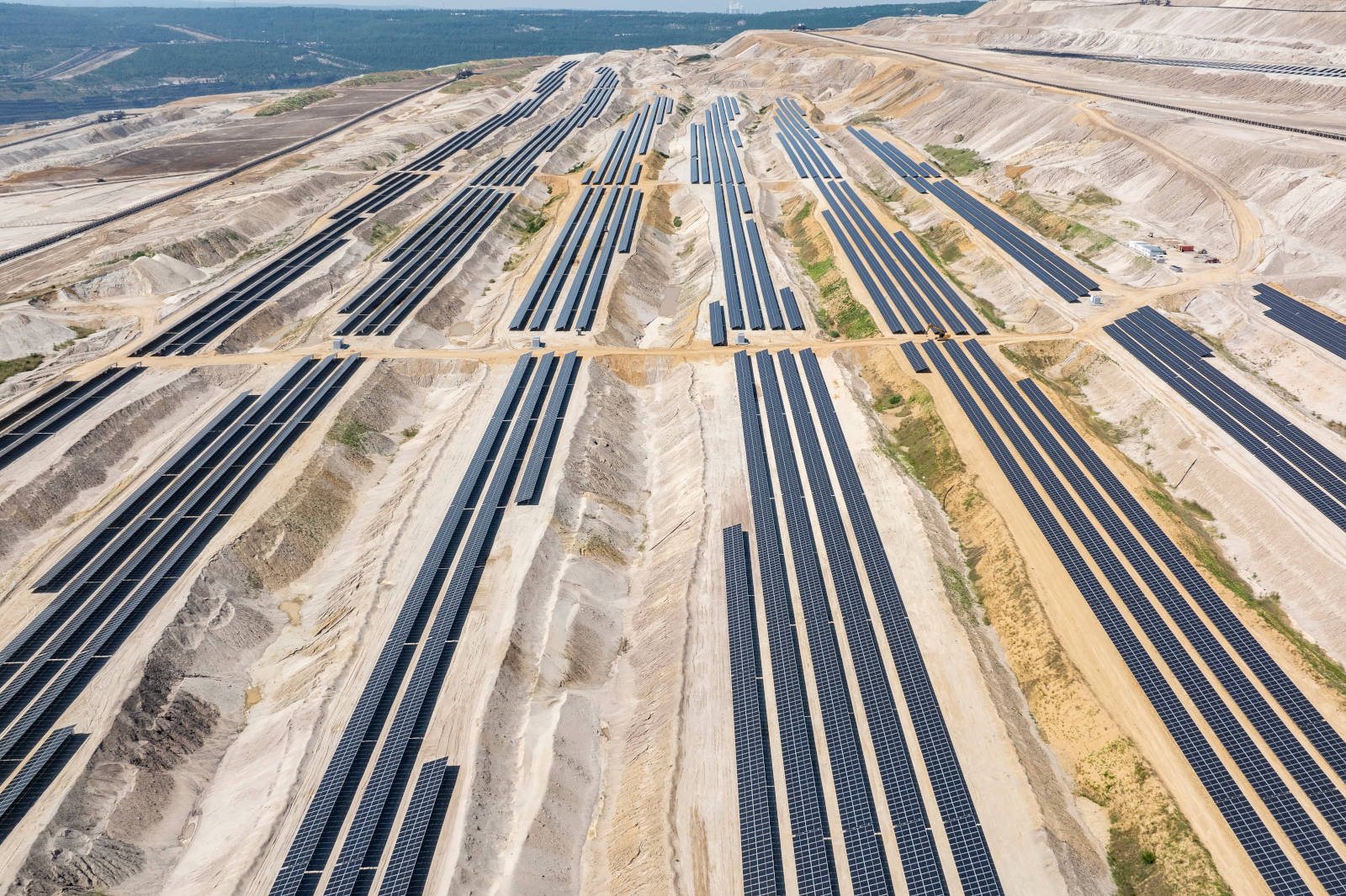 A large solar farm with numerous solar panels arranged in long rows across uneven terrain.
