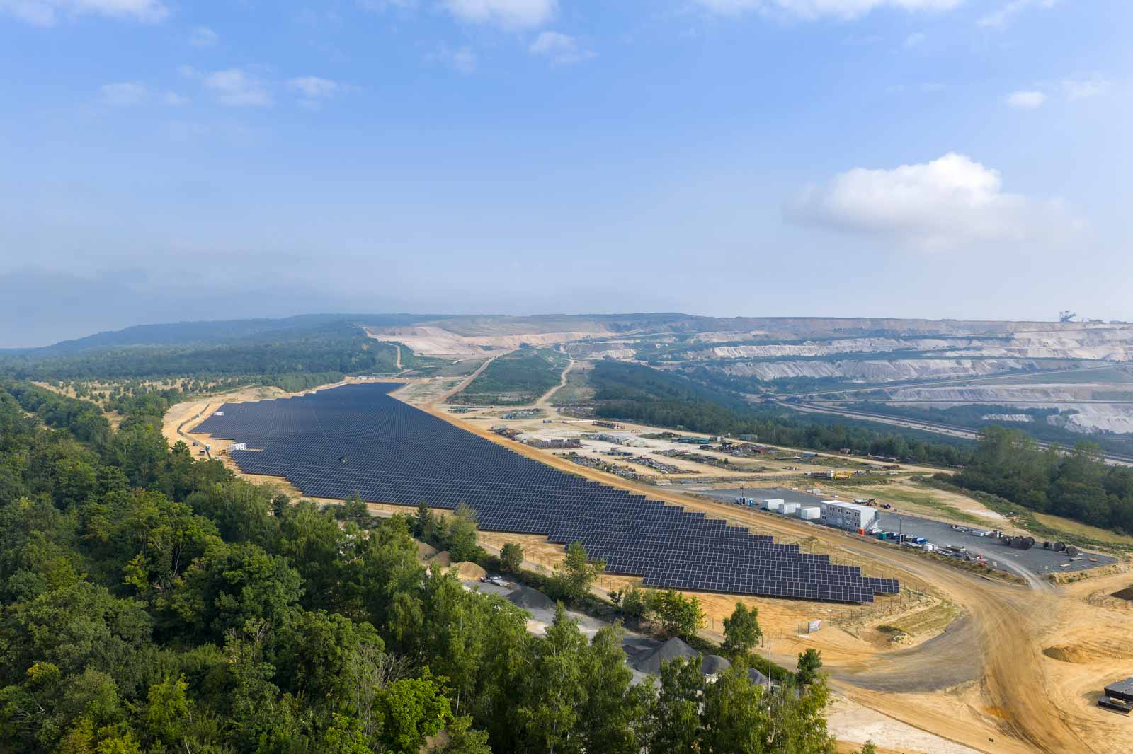 Eine große Solarfarm mit zahlreichen Solarpanelen, die in langen Reihen auf unebenem Gelände angeordnet sind.