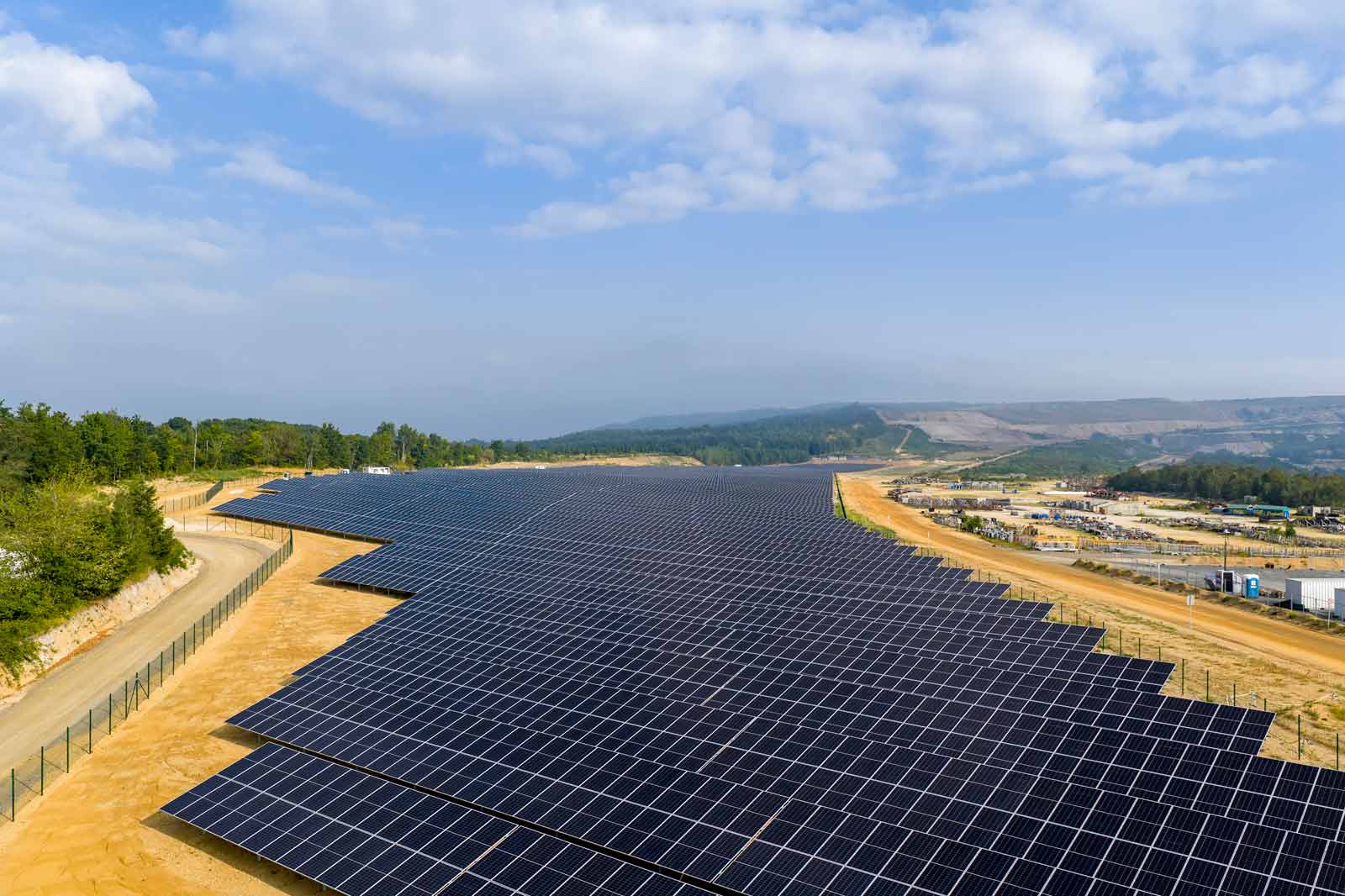 Eine große Solarfarm mit zahlreichen Solarpanelen, die in langen Reihen auf unebenem Gelände angeordnet sind.