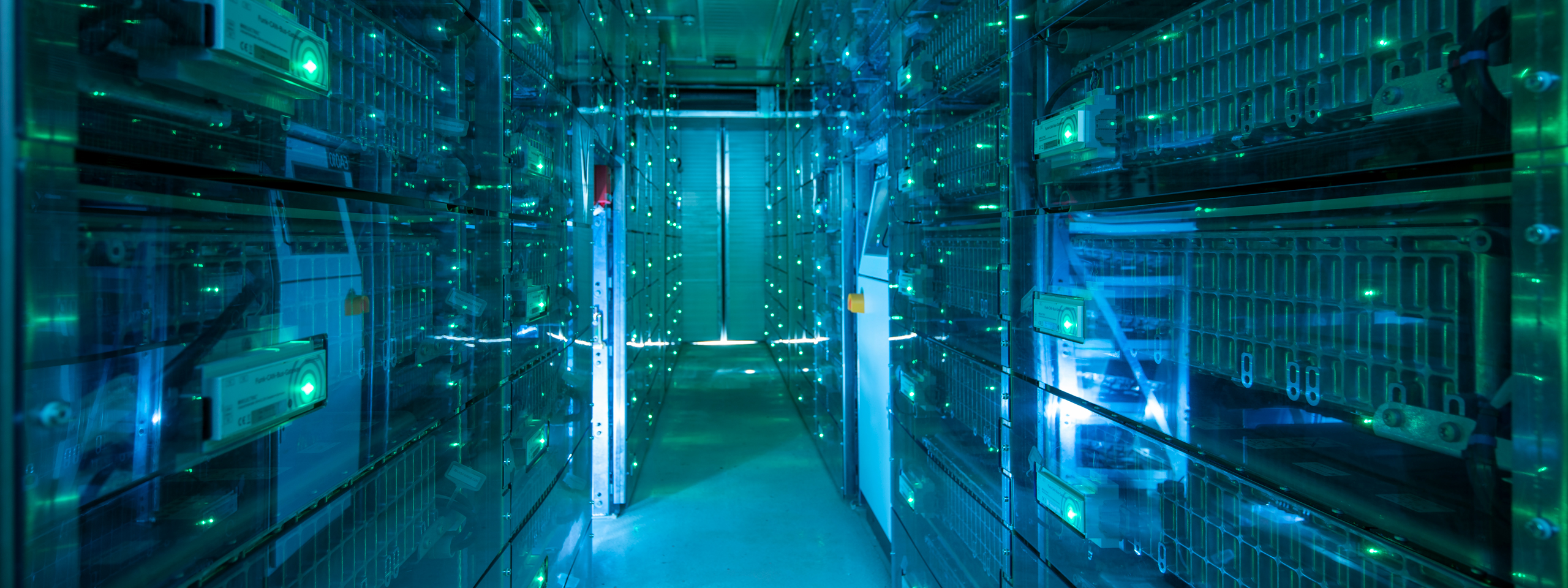 An illuminated corridor of server racks with blue and green lights in a data centre.