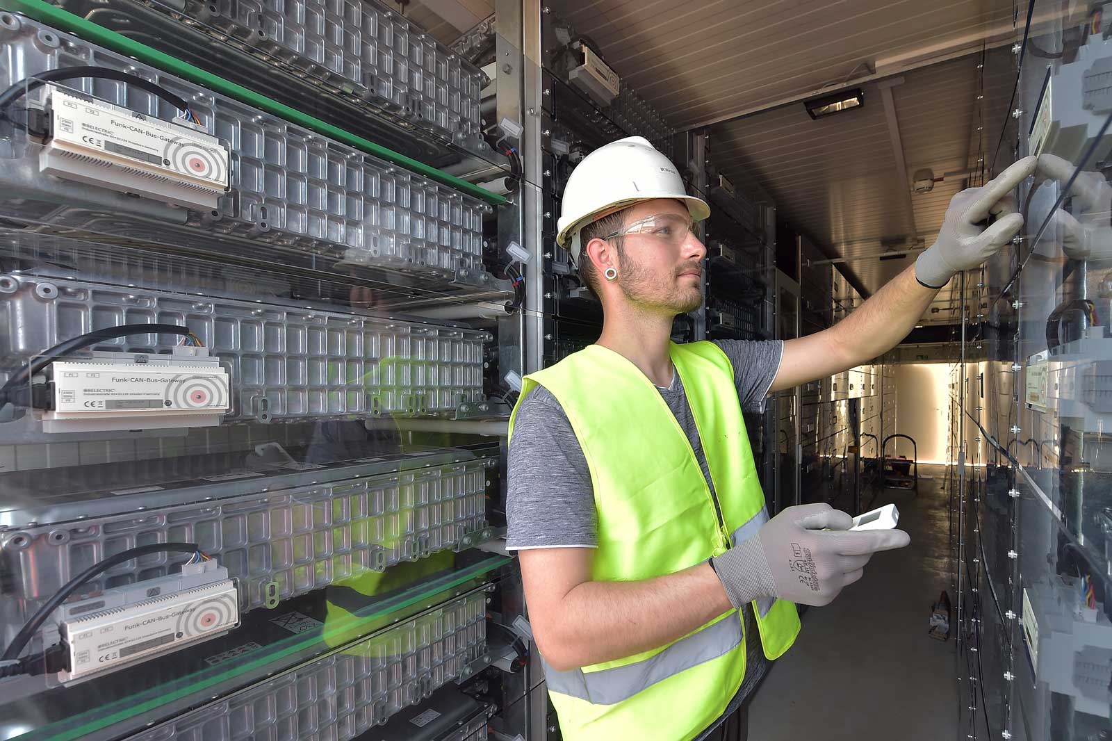 A worker in safety gear examines technical equipment in a modern storage space filled with battery modules.