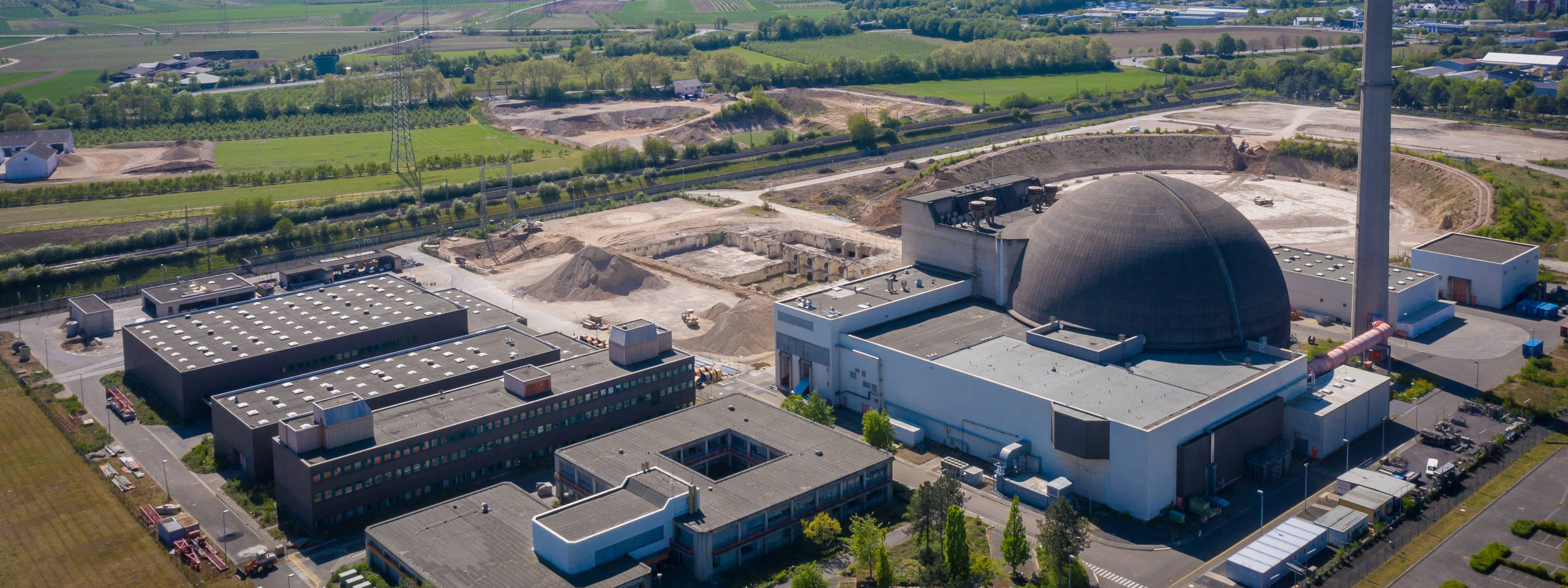 Luftaufnahme eines Kernkraftwerks mit einem großen, kuppelförmigen Gebäude und angrenzenden Bauarbeiten.