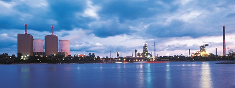 Eine industrielle Landschaft mit Kraftwerken und einer reflektierenden Wasseroberfläche unter bewölktem Himmel.