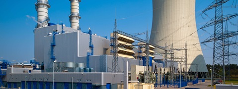 Ein Industriekomplex mit Kühlturm, Schornstein und elektrischen Anlagen unter klarem blauen Himmel.