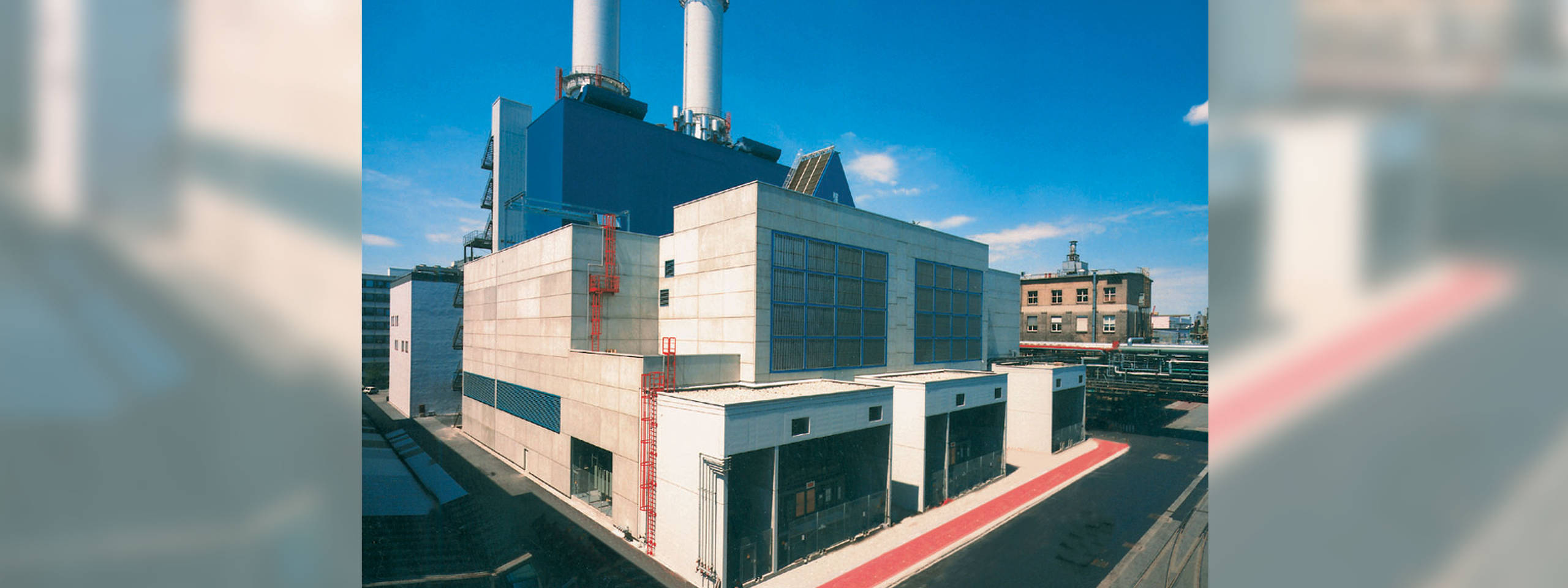 Ein modernes Industriegebäude mit zwei hohen Schornsteinen und einer grauen Fassade unter einem klaren blauen Himmel.