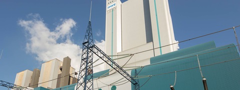 Ein blau-weißer Industriegebäudekomplex mit Stromleitungen und Wolken am Himmel.