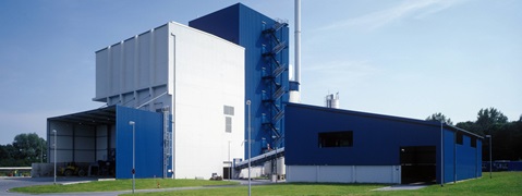 Ein modernes Industriegebäude mit blauer Fassade, großen Fenstern und einem hohen Schornstein vor einem klaren Himmel.